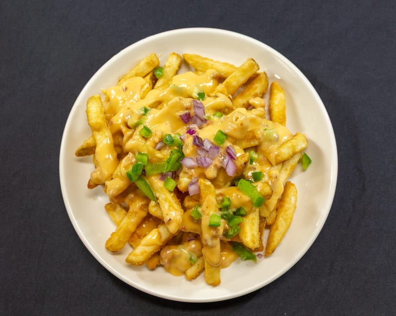 Golden french fries covered in melted cheese sauce, diced red onions, and green bell peppers.