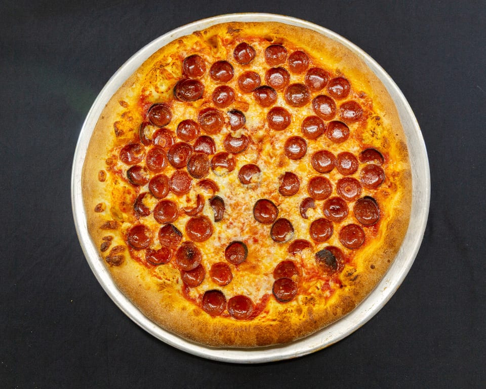 A freshly baked pepperoni pizza with a golden crust on a metal pan against a dark background.