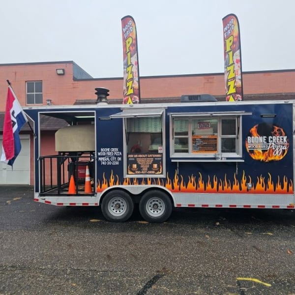 Boone Creek Wood Fired Pizza food truck, dark blue with flame decals, American flag, and pizza oven.