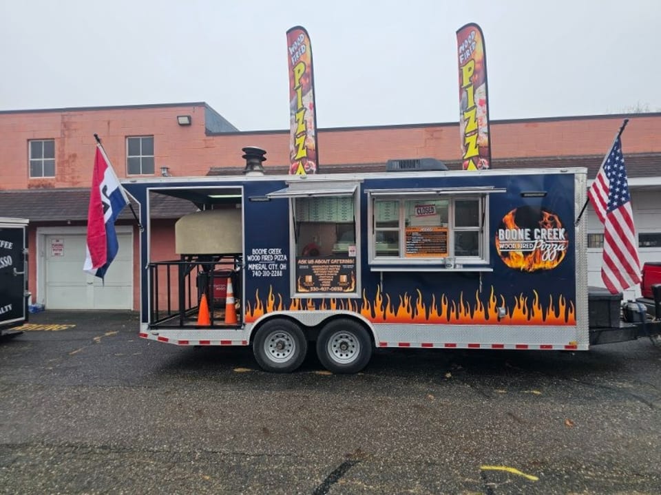 Boone Creek Wood Fired Pizza food truck, dark blue with flame decals, American flag, and pizza oven.