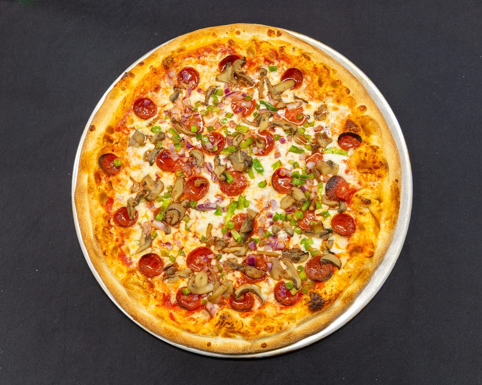 A whole pepperoni, mushroom, green pepper, and red onion pizza on a metal pan.