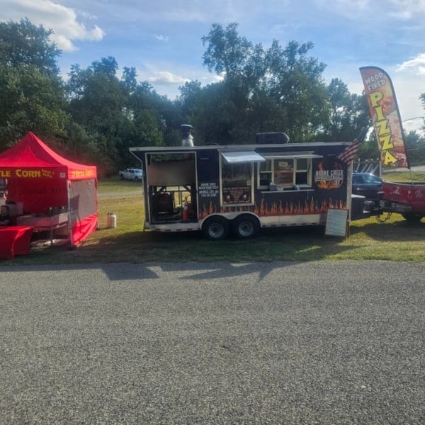A red kettle corn tent and a black food truck with flame decals parked on grass next to a road.