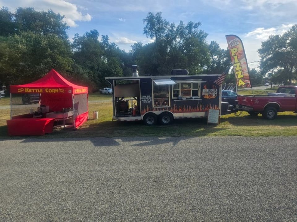 A red kettle corn tent and a black food truck with flame decals parked on grass next to a road.