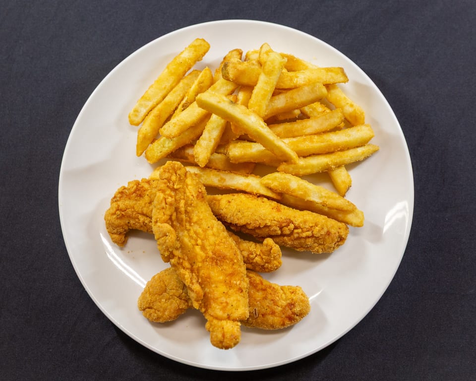 A white plate holds golden-brown fried chicken tenders and a pile of crispy french fries.