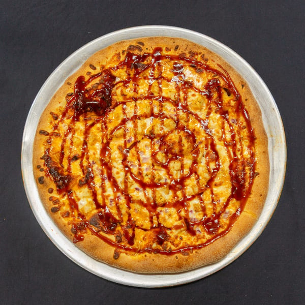 A BBQ chicken pizza with red onion and a swirl of barbecue sauce on a metal pan.