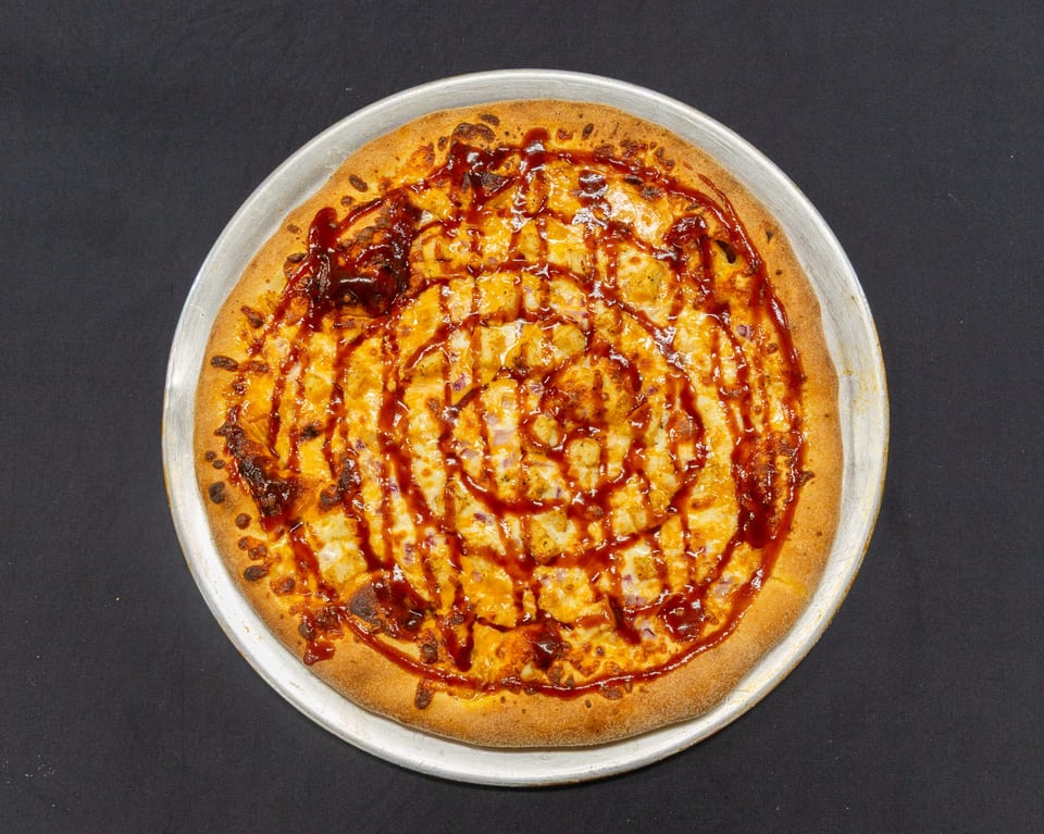 A BBQ chicken pizza with red onion and a swirl of barbecue sauce on a metal pan.