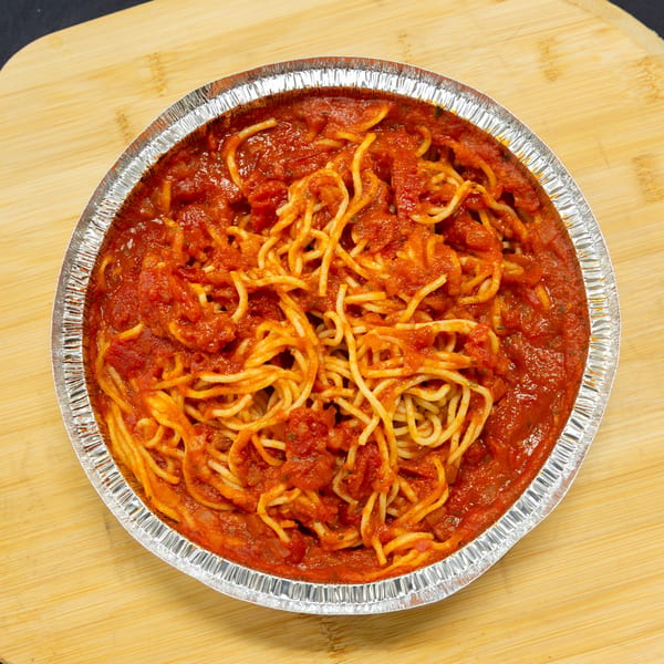 Spaghetti with red tomato sauce in a round aluminum takeout container on a wooden board.