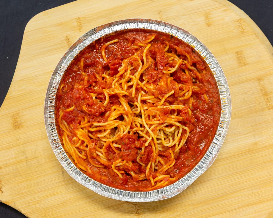 Spaghetti with red tomato sauce in a round aluminum takeout container on a wooden board.