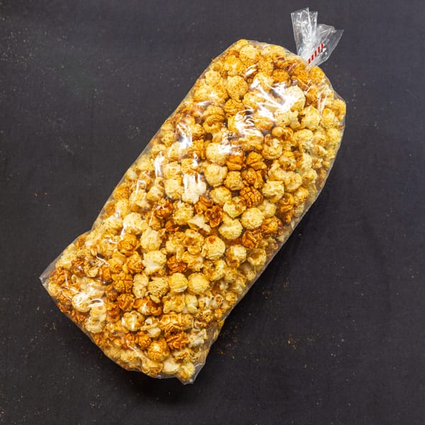 A clear plastic bag of caramel popcorn and regular popcorn on a dark surface.
