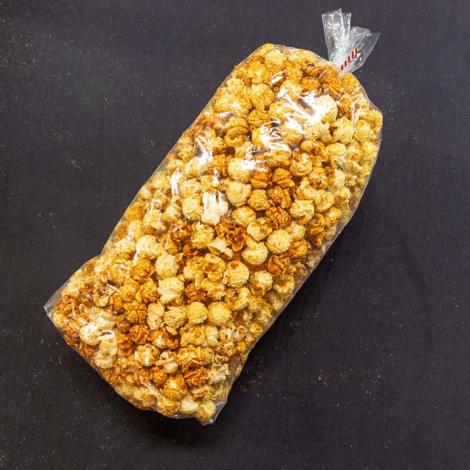 A clear plastic bag of caramel popcorn and regular popcorn on a dark surface.