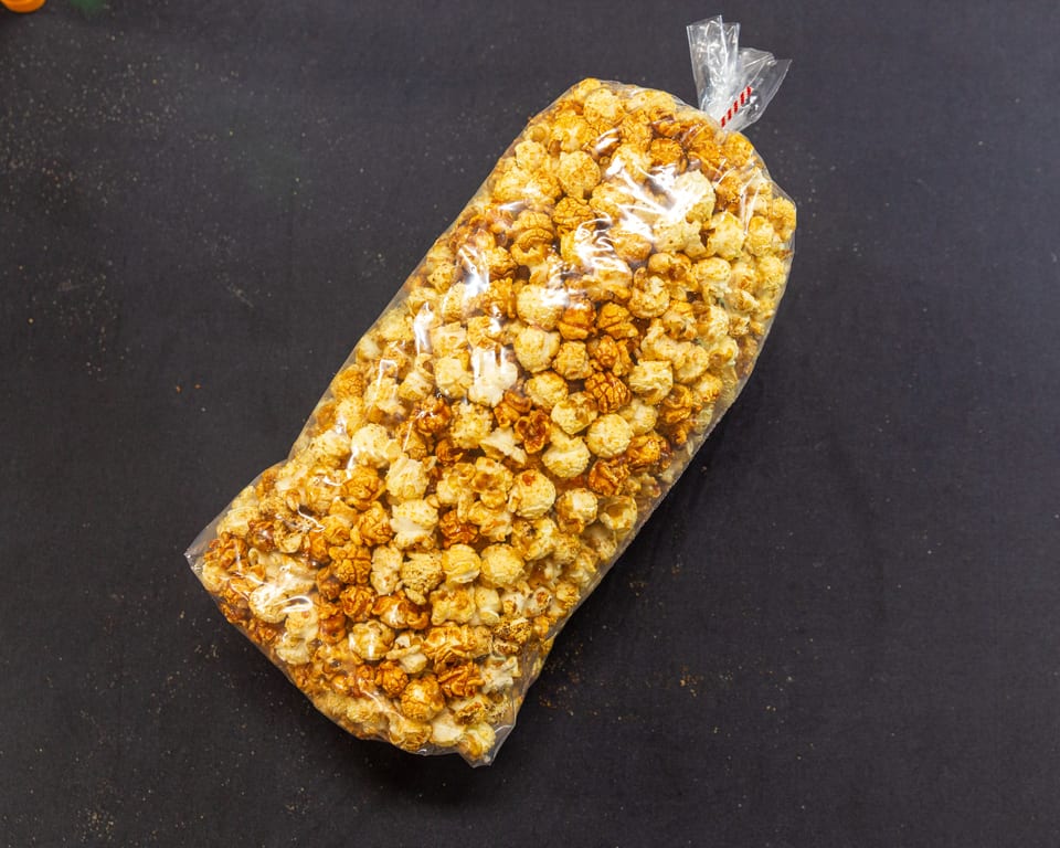 A clear plastic bag of caramel popcorn and regular popcorn on a dark surface.