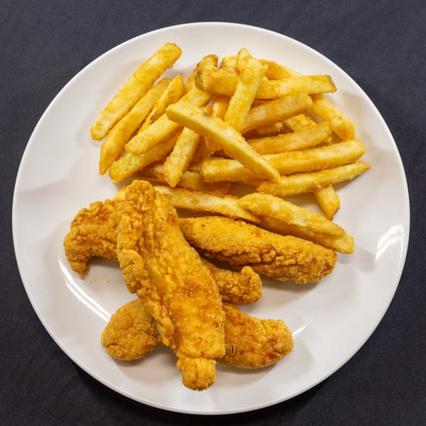 A white plate holds golden-brown french fries and crispy chicken tenders on a dark background.