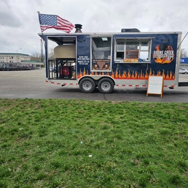 Boone Creek Wood Fired Pizza food truck with an American flag, parked in a lot.