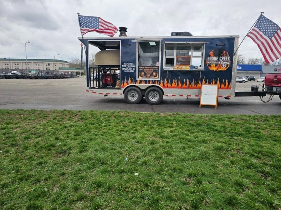 Boone Creek Wood Fired Pizza food truck with an American flag, parked in a lot.