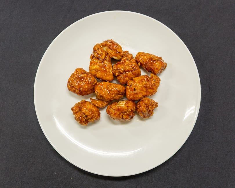 A white plate filled with golden-brown, glazed boneless chicken wings on a dark background.