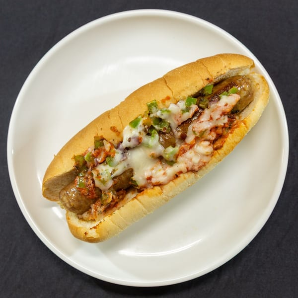 A sausage sandwich with melted cheese, green peppers, and red sauce on a white plate.