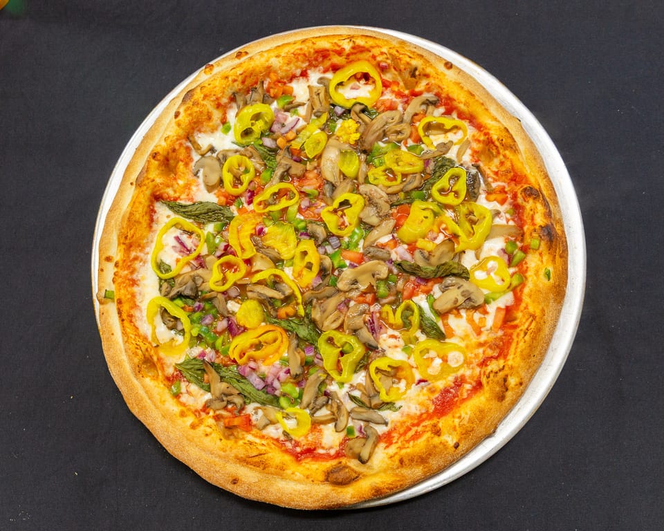 A vibrant veggie pizza with mushrooms, peppers, onions, and basil on a dark background.