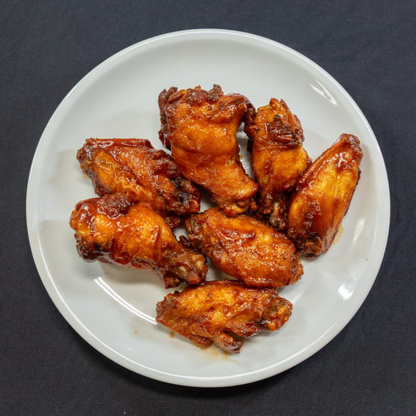 A white plate holds several glossy, golden-brown chicken wings coated in a rich, dark sauce.