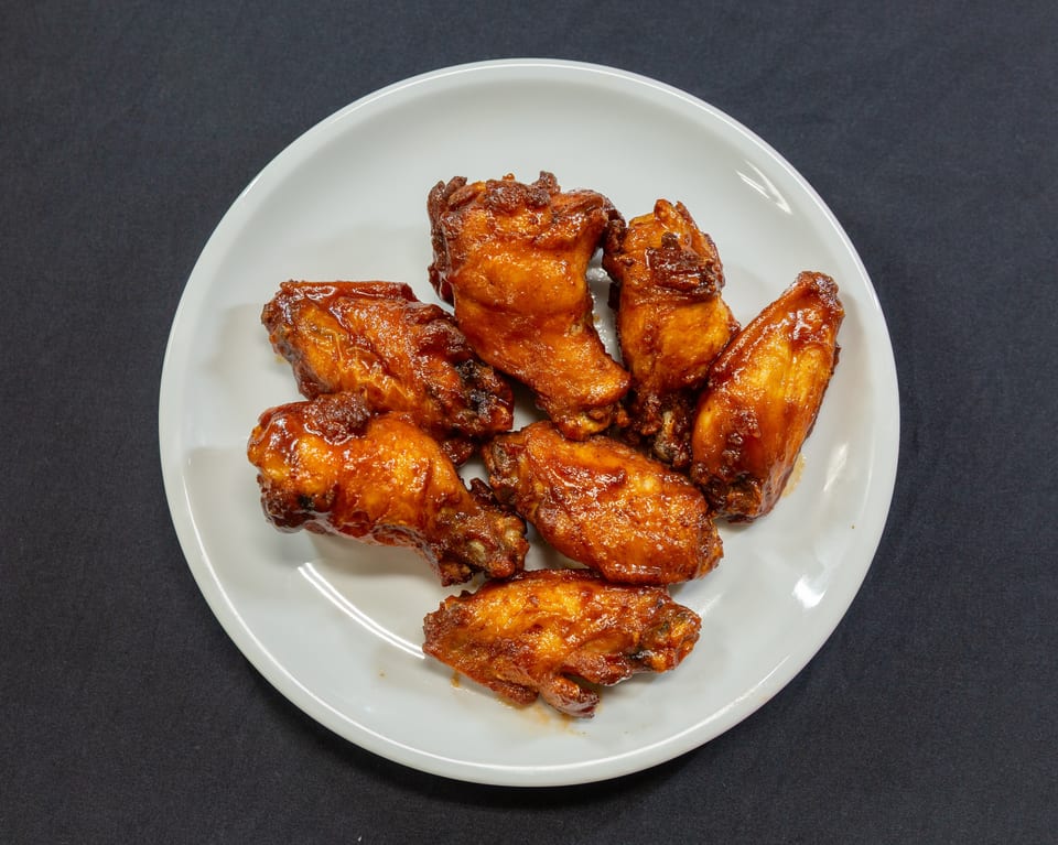 A white plate holds several glossy, golden-brown chicken wings coated in a rich, dark sauce.
