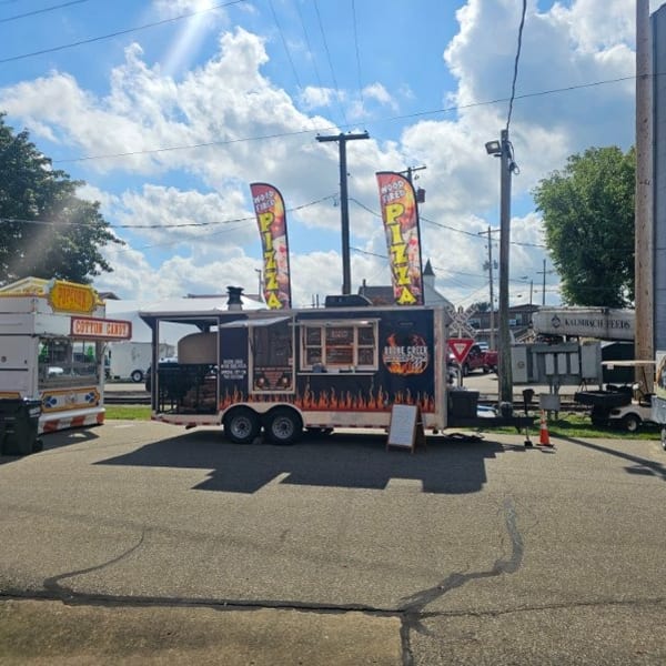 Boone Creek Pizza food truck with flame graphics, pizza flags, and a cotton candy stand nearby.