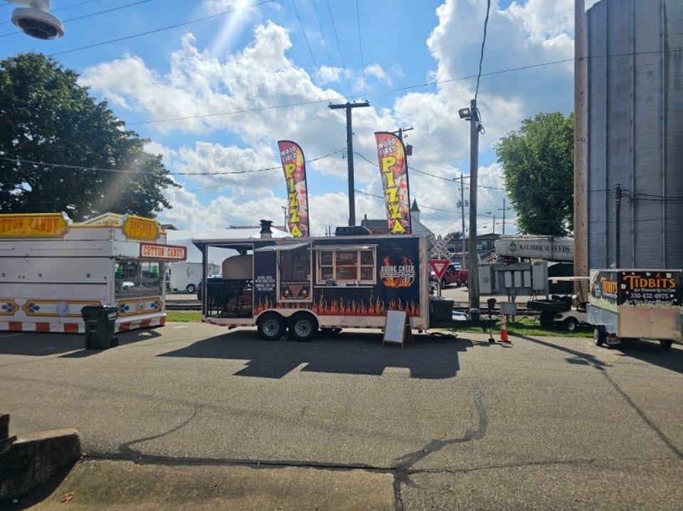 Boone Creek Pizza food truck with flame graphics, pizza flags, and a cotton candy stand nearby.