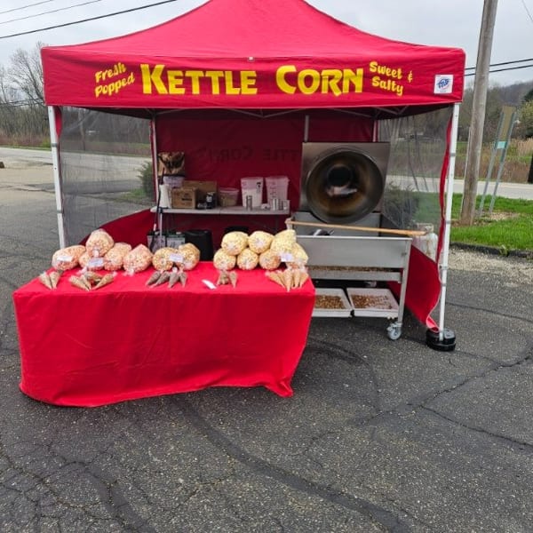 A red "Kettle Corn" tent with a popcorn machine and bags of kettle corn on a red table.