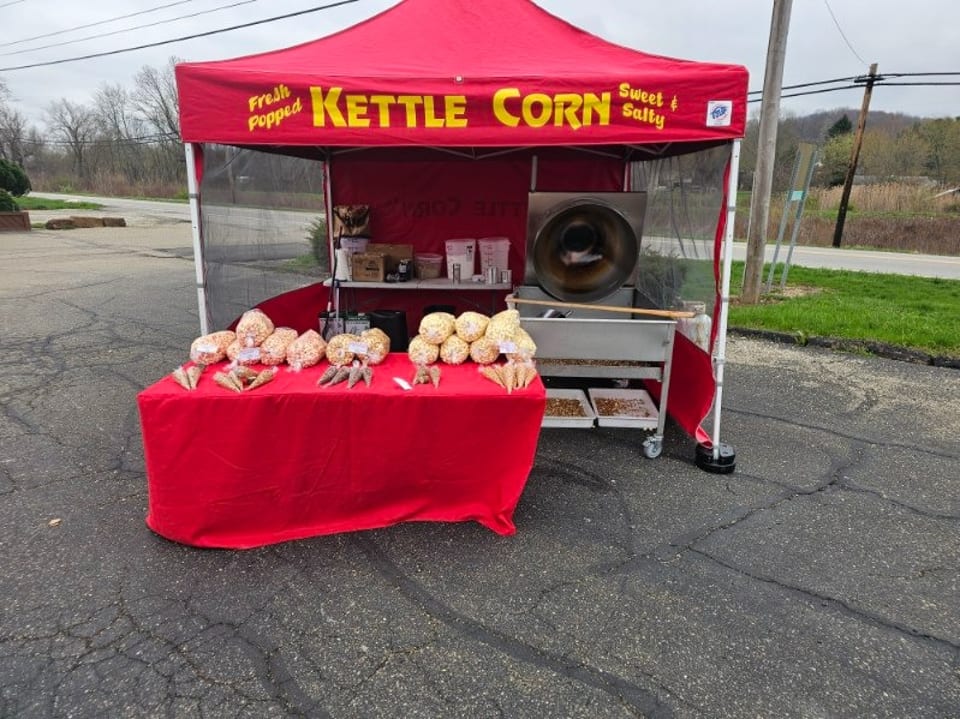 A red "Kettle Corn" tent with a popcorn machine and bags of kettle corn on a red table.