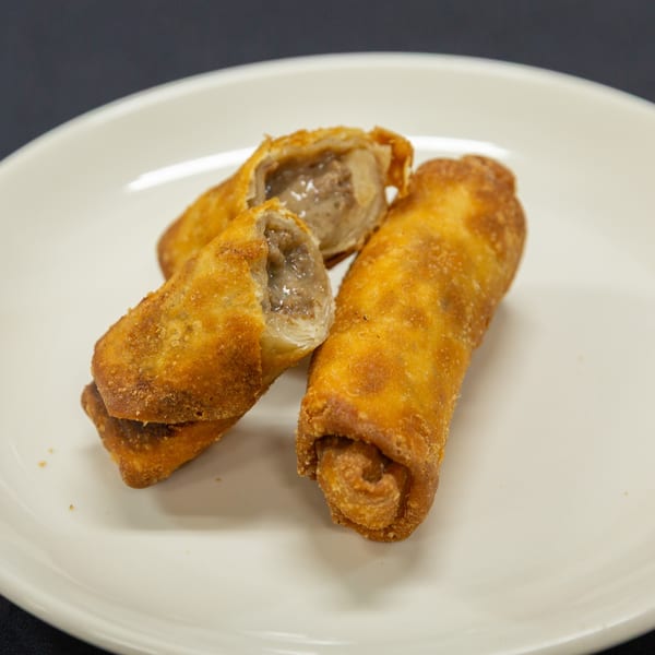 Three crispy fried egg rolls on a white plate, one cut open revealing a savory filling.