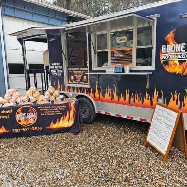 Boone Creek Wood Fired Pizza food truck with a catering table displaying popcorn and snacks.