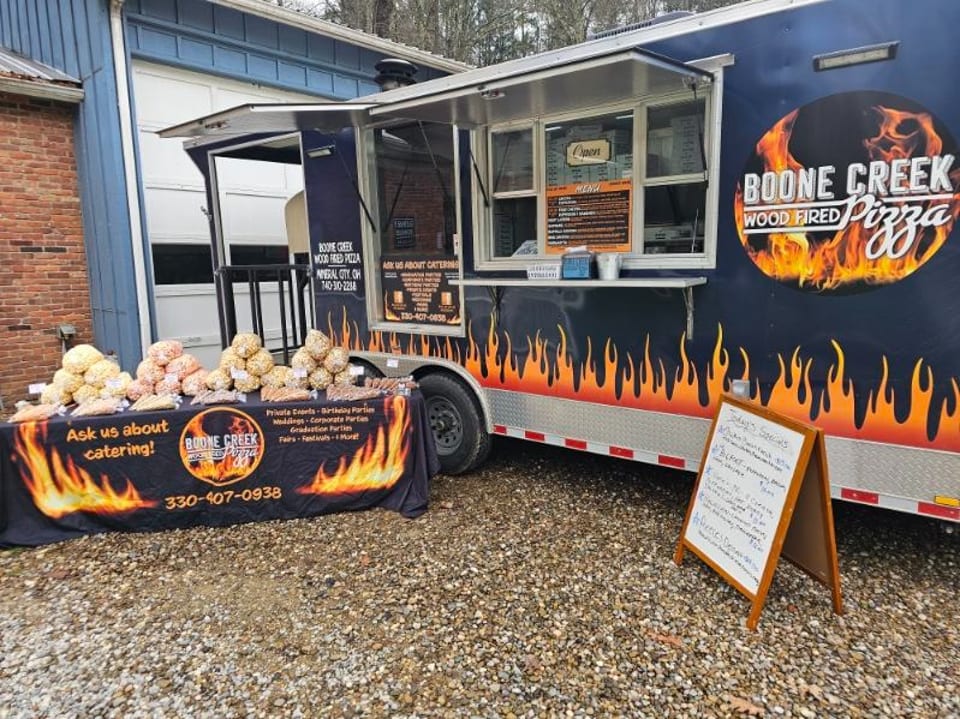 Boone Creek Wood Fired Pizza food truck with a catering table displaying popcorn and snacks.