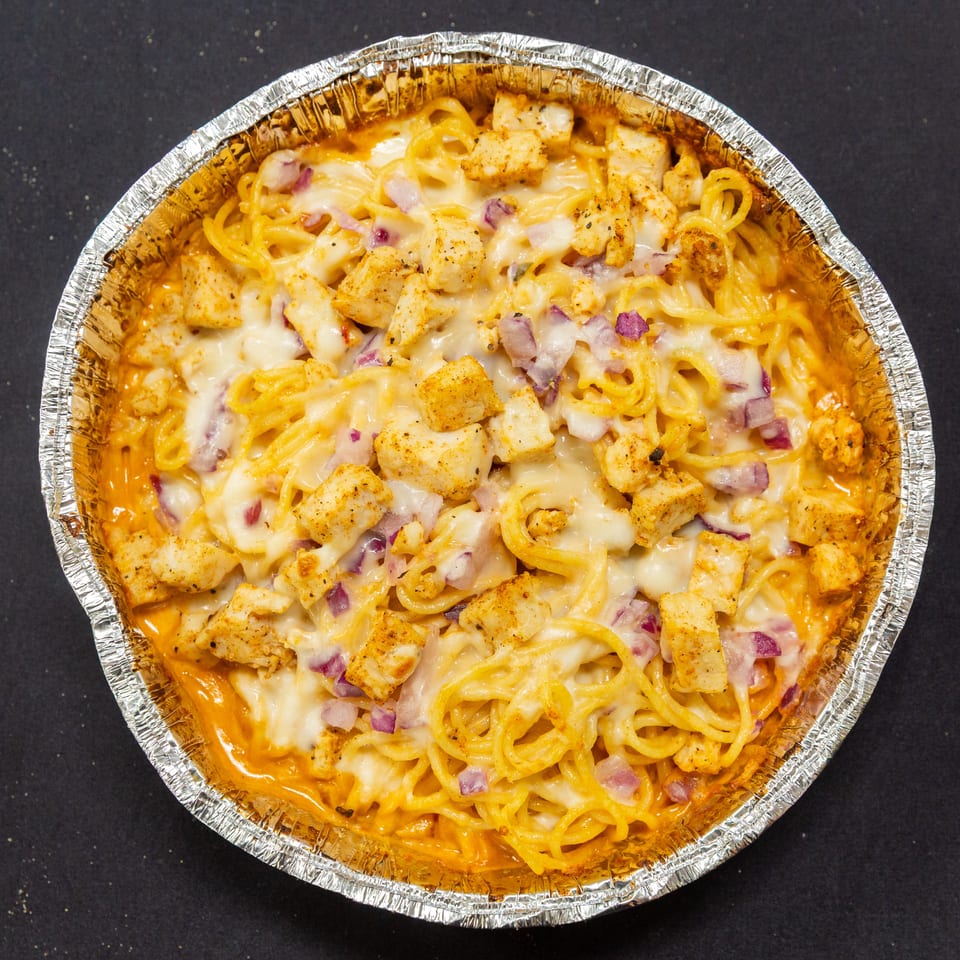 Baked spaghetti with chicken, red onions, and melted cheese in a foil pan.