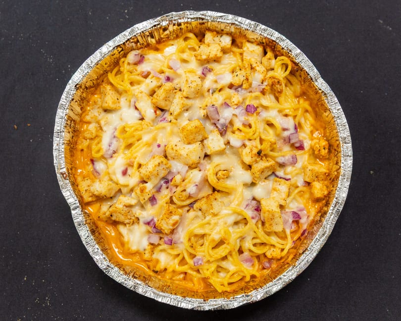 Baked spaghetti with chicken, red onions, and melted cheese in a foil pan.