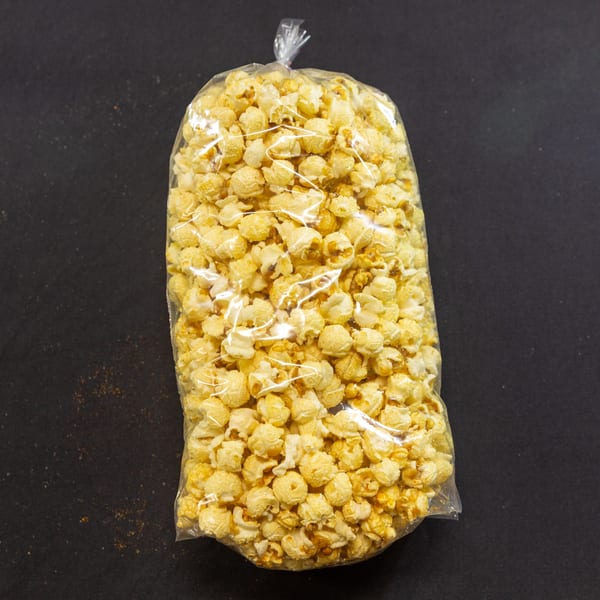 A clear plastic bag filled with golden caramel popcorn sits on a dark, textured surface.