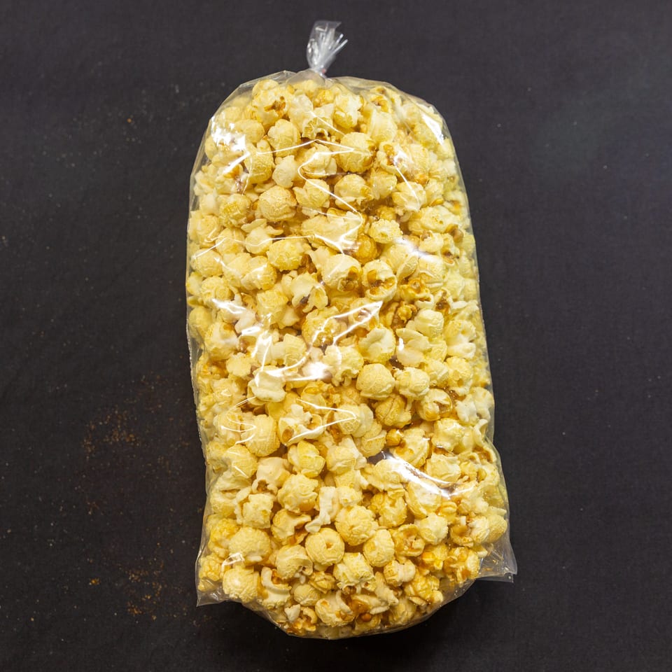 A clear plastic bag filled with golden caramel popcorn sits on a dark, textured surface.