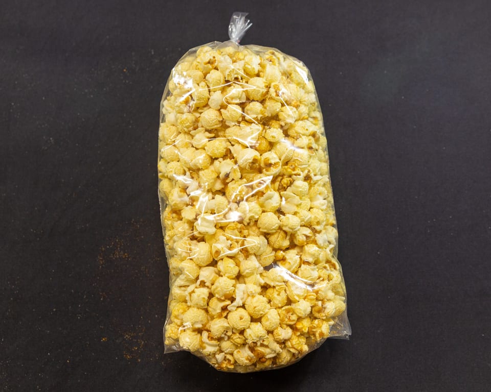 A clear plastic bag filled with golden caramel popcorn sits on a dark, textured surface.