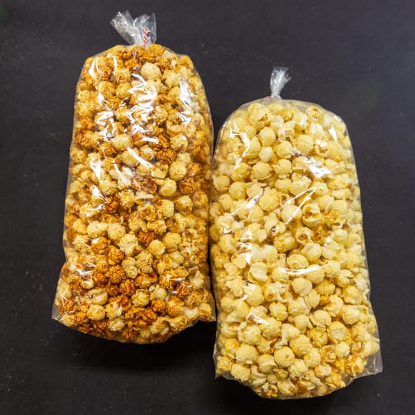 Two clear bags of popcorn, one caramel and one butter, on a dark surface.