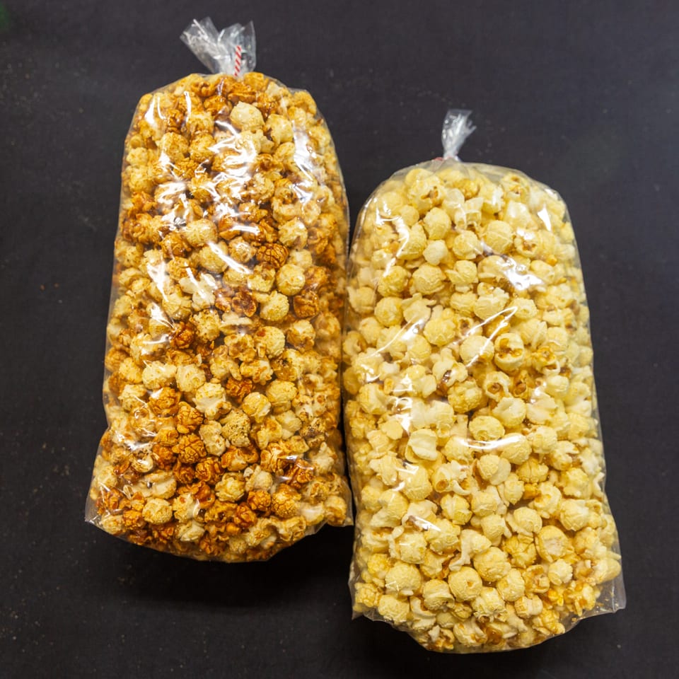 Two clear bags of popcorn, one caramel and one butter, on a dark surface.
