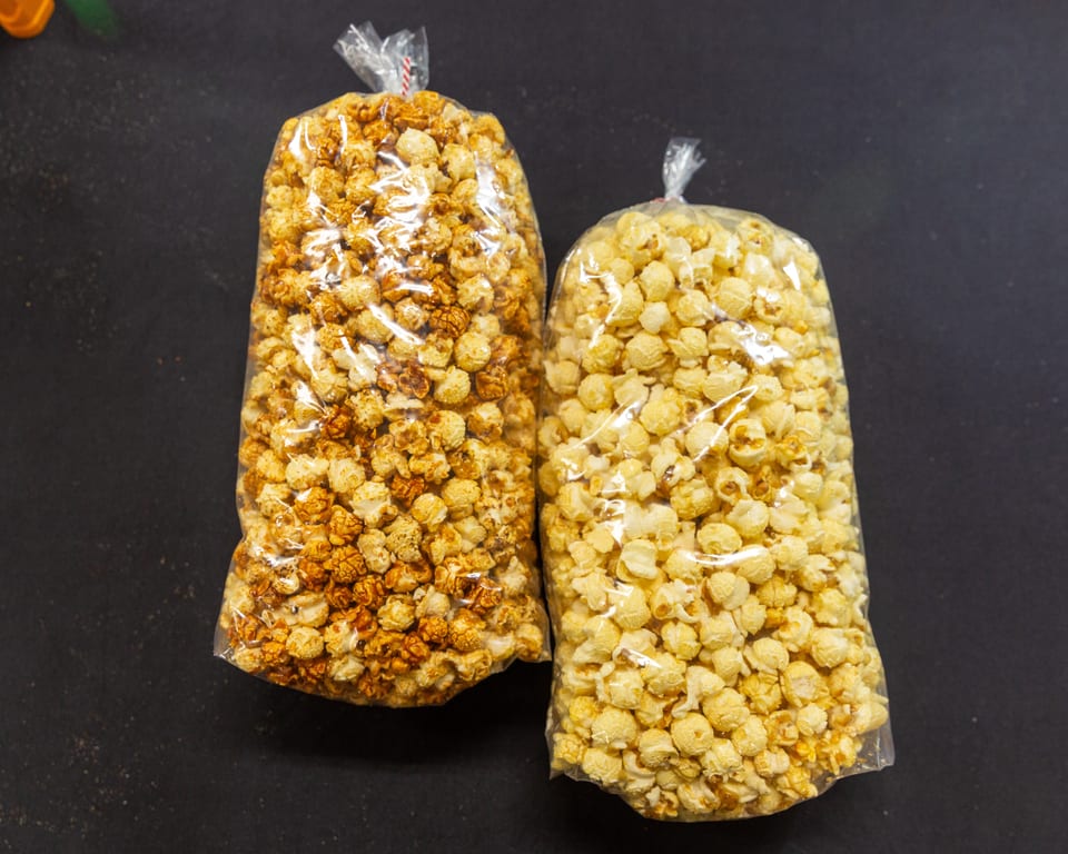 Two clear bags of popcorn, one caramel and one butter, on a dark surface.