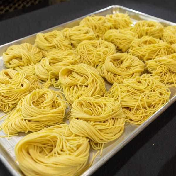 Bundles of fresh, uncooked yellow noodles are arranged on a silver baking sheet.