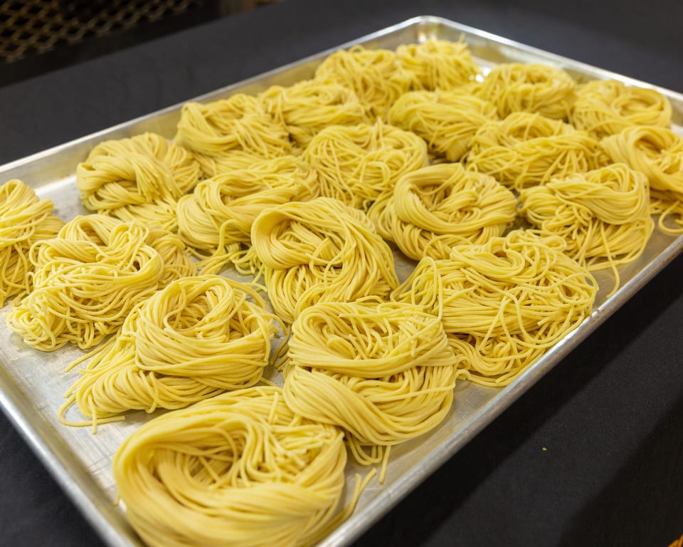 Bundles of fresh, uncooked yellow noodles are arranged on a silver baking sheet.