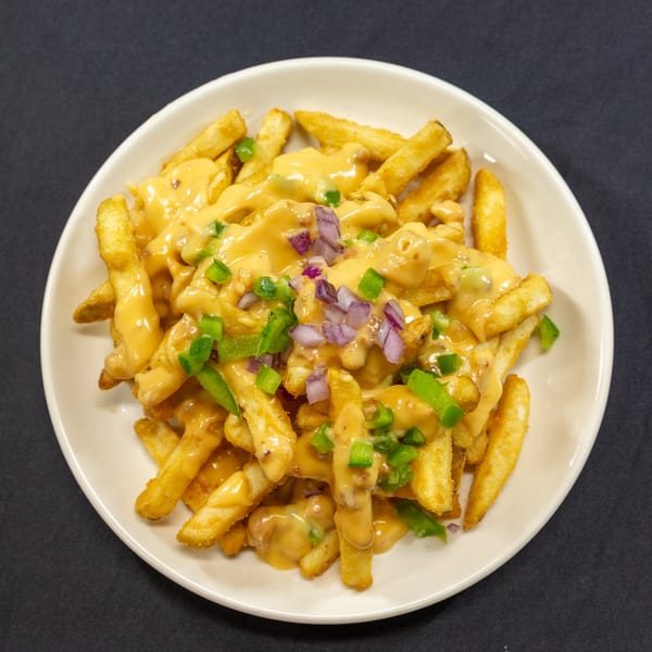 Golden french fries covered in melted cheese sauce, diced red onions, and green peppers on a white plate.