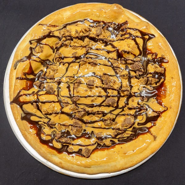 Dessert pizza with peanut butter, chocolate drizzle, and peanut butter cup crumbles.