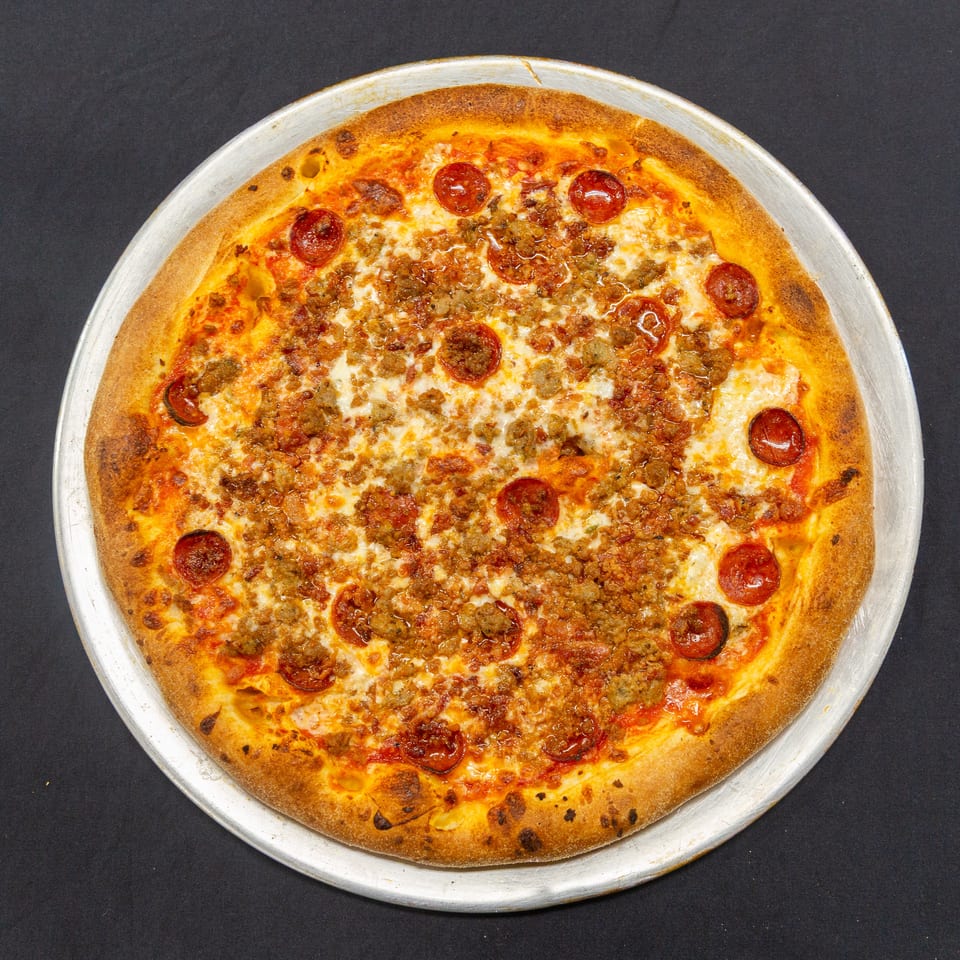 A whole pepperoni and sausage pizza on a metal tray, viewed from directly above.