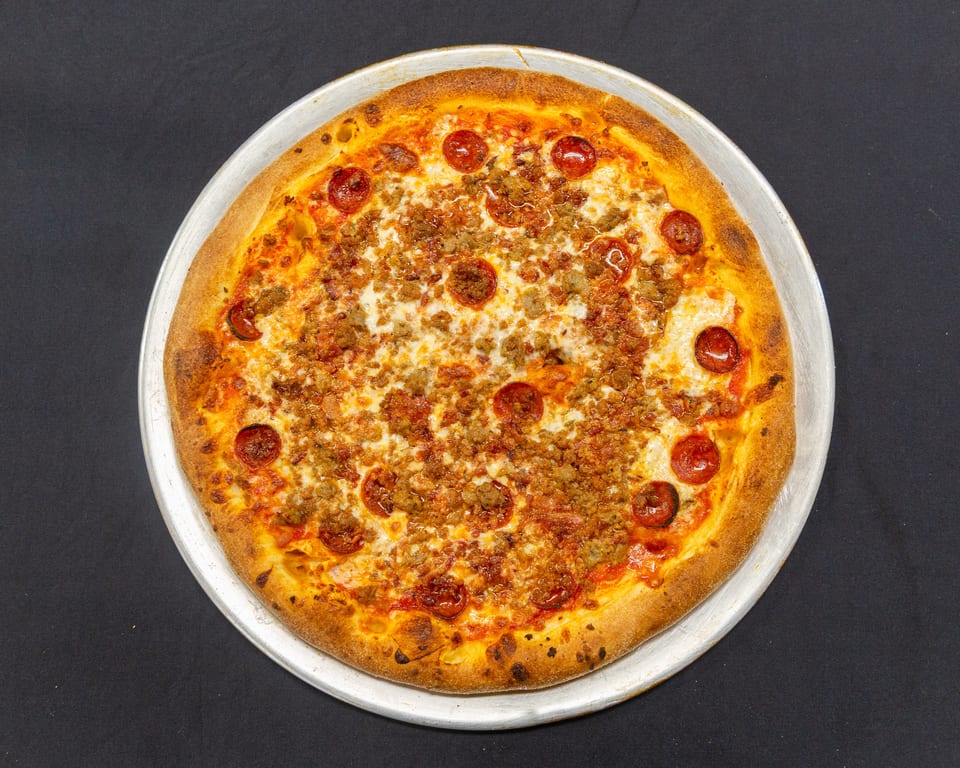 A whole pepperoni and sausage pizza on a metal tray, viewed from directly above.