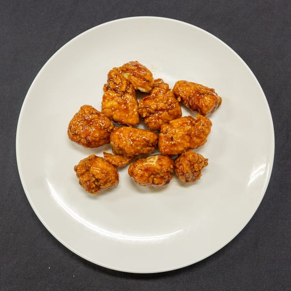 A white plate filled with golden-brown, glazed boneless chicken wings on a dark background.
