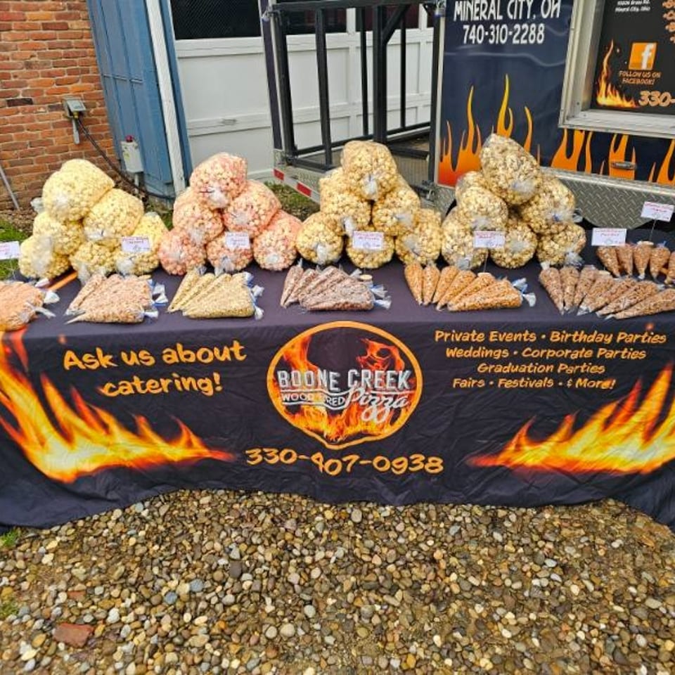 Boone Creek Wood Fired Pizza catering table with various popcorn bags and cones.