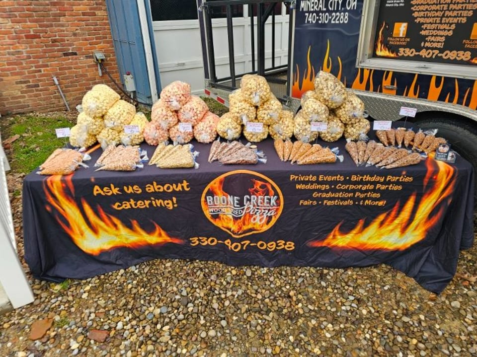 Boone Creek Wood Fired Pizza catering table with various popcorn bags and cones.