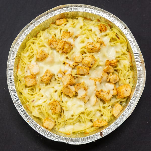 Baked spaghetti with melted cheese and seasoned chicken pieces in a foil pan.