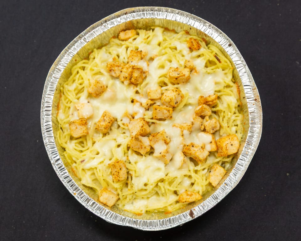 Baked spaghetti with melted cheese and seasoned chicken pieces in a foil pan.