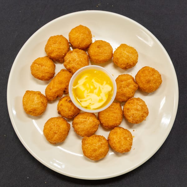 A white plate filled with golden-brown fried cheese balls and a small cup of melted cheese sauce.